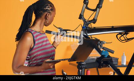 Engineer doing bike servicing in studio background repair shop, searching replacement components online on laptop. Professional looking for necessary work tools for repairing bicycle Stock Photo
