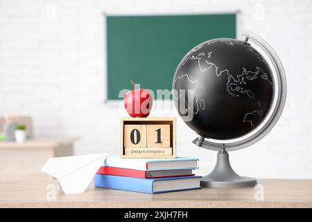 Apple, books, globe and cube calendar with date SEPTEMBER 1 on desk in classroom. Back to school concept Stock Photo