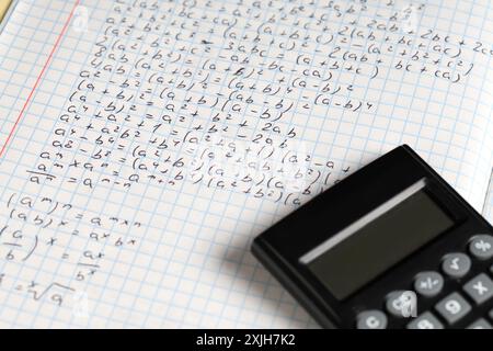 Copybook with handwritten maths formulas and calculator as background, closeup Stock Photo