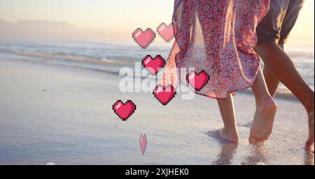 Image of hearts moving over legs of diverse couple in love on beach in summer Stock Photo