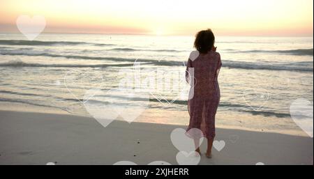 Image of hearts moving over diverse couple in love on beach in summer. Love, romance, valentine's day and vacation concept digitally generated image. Stock Photo