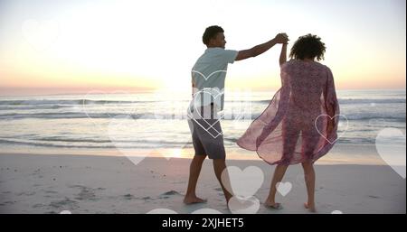 Image of hearts moving over diverse couple in love on beach in summer. Love, romance, valentine's day and vacation concept digitally generated image. Stock Photo