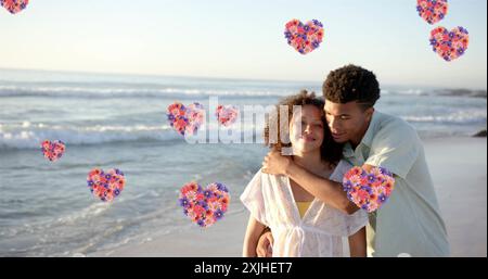 Image of hearts moving over diverse couple in love on beach in summer. Love, romance, valentine's day and vacation concept digitally generated image. Stock Photo