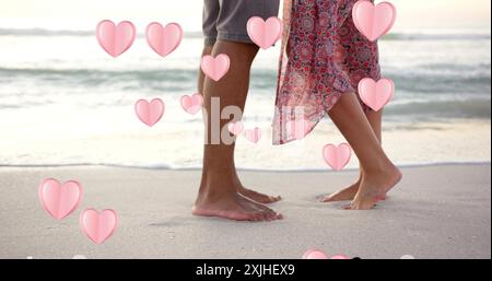 Image of hearts moving over legs of diverse couple in love on beach in summer Stock Photo