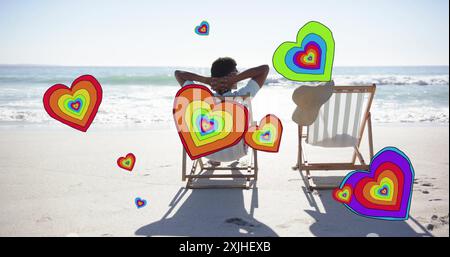 Image of hearts moving over diverse couple in love in deckchairs on beach in summer Stock Photo