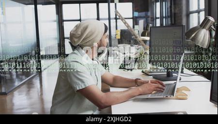 Image of binary coding and data processing over biracial businessman in office. Global finance, business, connections, computing and data processing c Stock Photo