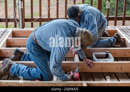 Two senior men, in their 80s, on their knees building a wooden frame for an exterior wall for a small house, USA. Stock Photo