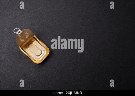 Tin or aluminum opened rectangular can of canned food with a key on a dark concrete background Stock Photo