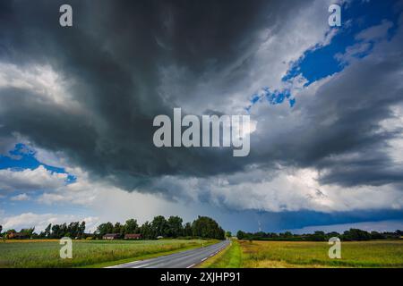 Storm clouds loom over rural landscape, creating a dramatic scene as a car drives down the road Stock Photo