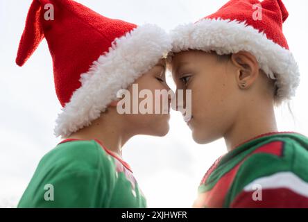 two cute children in Santa hats in profile pressed their noses to each other on a light background. Boys dream on Christmas Eve, expecting gifts and m Stock Photo