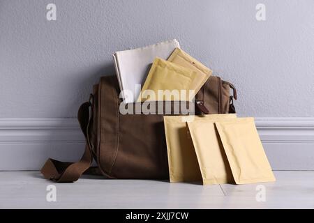 Brown postman's bag with envelopes and newspapers near grey wall Stock Photo