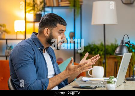 Angry furious Indian man freelancer using laptop while working at home office table having nervous breakdown at work, stress management, mental distress problems, losing temper, reaction on failure. Stock Photo