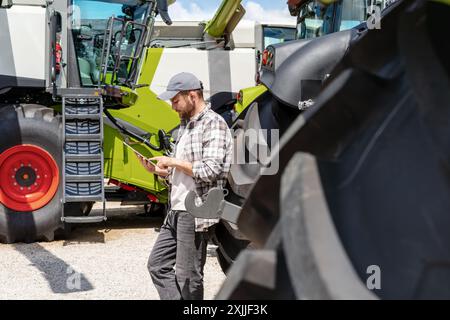 Man wearing casual clothing stands at agricultural equipment dealer and using his digital tablet. Stock Photo