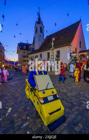 Lucerne, Switzerland - February 20, 2023: People in costumes and other crowd, near the St. Peter Chapel, at sunrise, part of the Fasnacht Carnival, in Stock Photo