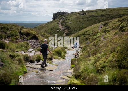 Walkers make their way off Kinder Scout plateau and on towards Crowden Tower on the lower stages of the Pennine Way, on 17th July 2024, in Edale, Derbyshire, England. Stock Photo