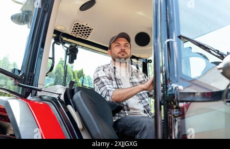 An adult bearded man in a plaid shirt and cap drives a construction or agricultural machine. Stock Photo