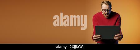 Stylish man in a red sweater interacting with a black laptop. Stock Photo