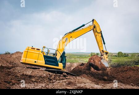 Excavator moving loose soil in an open field. Stock Photo
