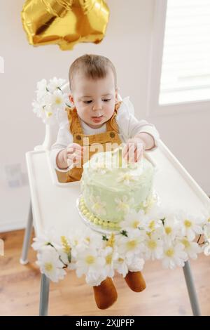 Baby enjoying first birthday cake with gold balloon and floral decor Stock Photo