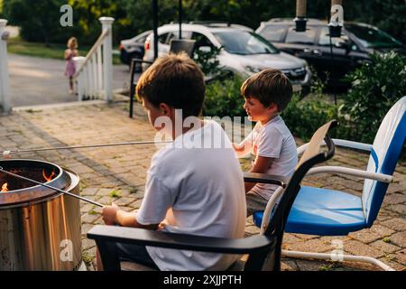 Boys roasting marshmallows on fire pit in backyard patio Stock Photo