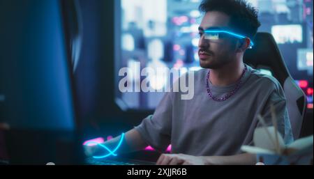 Handsome Influencer Working on Computer in His Stylish Sci-Fi Studio. Young Creative Genius Developing Innovative Software Technology. Man Wearing Futuristic Monocle Glasses with Extended Reality Stock Photo