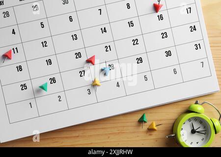 Timetable. Calendar page, drawing pins and alarm clock on wooden table, top view Stock Photo