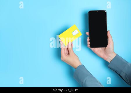 Woman holding SIM card and smartphone on light blue background, closeup. Space for text Stock Photo