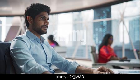 Close-Up of a Young Indian Male Professional Working in a Business Research and Development Company. Handsome Manager Analyzing Financial Reports, Looking at a Computer Screen with Graphs and Charts Stock Photo