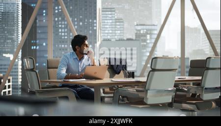 Portrait of a Young Indian Account Manager Working on a Laptop Computer in a Modern Corporate Office. Businessman Dealing with Financial Reports, Preparing a Growth Plan for the Company Stock Photo