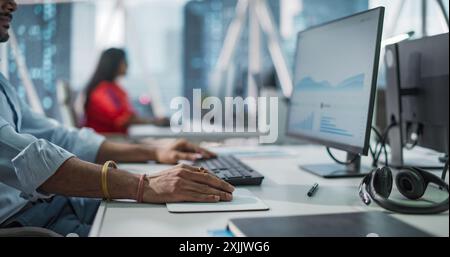 Close Up of a Young Indian Male Professional Working in a Business Research and Development Company. Handsome Manager Analyzing Financial Reports, Looking at a Computer Screen with Graphs and Charts Stock Photo