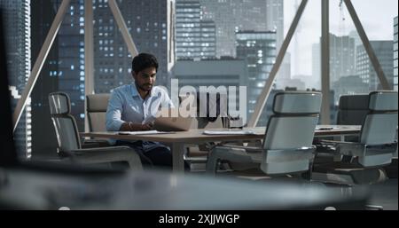 Indian Executive Manager Working in a Business Research and Development Office on a Laptop Computer. Focused South Asian CEO Reviewing Corporate Growth Strategy and Communicating with Partners Stock Photo