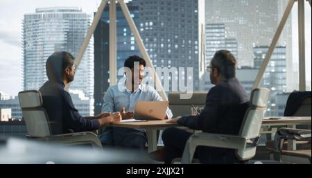 Three Young South Asian Colleagues Working in a Business Software Development Company. Indian Team Leader Using Laptop Computer, Updating Corporate Partners on Financial Market News and Trends Stock Photo