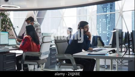 Young Team of Indian Specialists Working on Computers and Having a Conversation in the Office. Male and Female Colleagues Discussing a Solution for Their Generative Artificial Intelligence Project Stock Photo