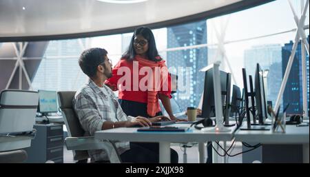 Two Young Indian Financial Advisers Having a Conversation About Stock Market Strategy Next to a Computer in a Modern Company. South Asian Managers Work in a Banking Research and Development Center Stock Photo