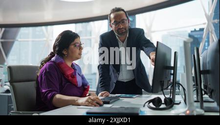 Financial Analyst Having a Meeting to Discuss a Business Project with a Handsome Indian Team Leader. South Asians Colleagues Using Desktop Computer, Comparing Reports and Data in a Modern Office Stock Photo