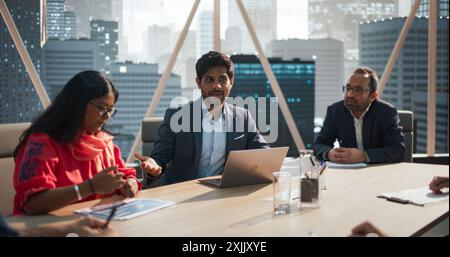 Office Meeting in a Conference Room: Handsome Indian Specialist Talking About a Company Strategy with Diverse Team of Businesspeople. Ambitious, Creative Start-up Team Discussing Financial Reports Stock Photo