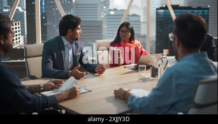 Indian Female Project Manager Makes a Business Presentation for a Diverse Creative Team in a Meeting Room in an Agency. South Asian Colleagues Gathered Around a Conference Table. Stock Photo