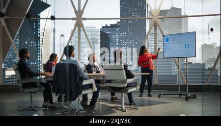 Diverse Indian Office Conference Room: Young South Asian Female CEO Makes a Presentation for Entrepreneurs, Talking, Using TV with Infographics and Statistics. Businesspeople Discussing Reports Stock Photo