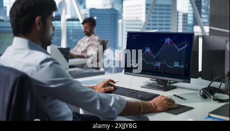 Hedge Fund Office: Indian Financial Analyst Using Computer with Display Showing Real-Time Stocks, Exchange Market Charts. Hard Working South Asian Trader Making Profitable Investment. Stock Photo