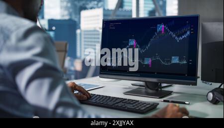 Hedge Fund Office: Indian Financial Analyst Using Computer with Display Showing Real-Time Stocks, Exchange Market Charts. Hard Working South Asian Trader Making Profitable Trade. Stock Photo