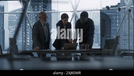 Three Diverse Colleagues Entering Office Meeting Room To Discuss Business Strategy. Male And Female Specialists Using Laptop, Working On Innovative Technological Project. Dramatic Evening Edit. Stock Photo