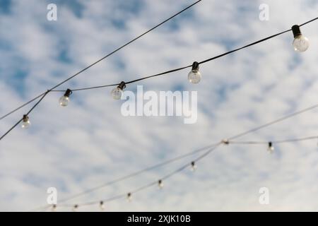 Light bulbs on a wire against the blue sky with white clouds Stock Photo