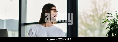 Handsome businessman with long hair stands contemplatively in front of a window. Stock Photo