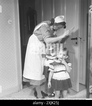 Maid 1949. A young woman employed as a nanny and maid is in the kitchen with the family's two little girls. The girls are nicely dressed in similar dresses and the nanny brushes their hair. 1949. Kristoffersson ref AX31-11 Stock Photo