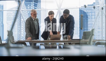 Three Diverse Colleagues Entering Big City Office Meeting Room To Discuss Business Strategy. Male And Female Specialists Talking, Using Laptop Computer, Working On Innovative Technological Project. Stock Photo