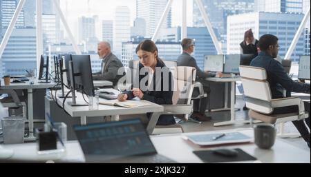 In Big Corporate Skyscraper Office: Beautiful Caucasian Female Business Manager Using Computer, Businesspeople and Experts Working Around Her, Analysing Statistics, Commerce Data, and Marketing Plans. Stock Photo
