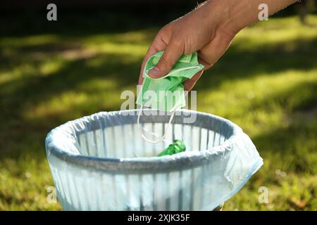 Man throwing medical mask into garbage bin outdoors, closeup Stock Photo