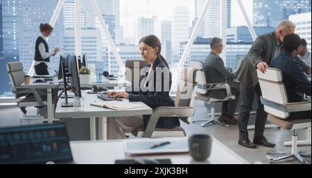In Big Corporate Skyscraper Office: Beautiful Caucasian Female Business Manager Using Computer, Businesspeople and Experts Working Around Her, Analysing Statistics, Commerce Data, Marketing Plans. Stock Photo