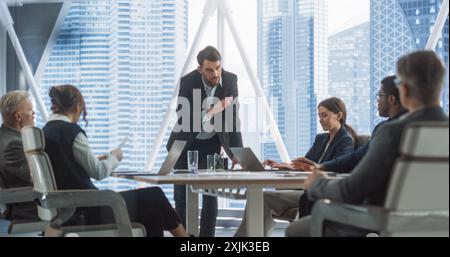 Office Conference Room Meeting Presentation: Caucasian Businessman Talks, Uses Green Screen Chroma Key TV Set. Male CEO Successfully Presenting a e-Commerce Product to Group of Multi-Ethnic Investors. Stock Photo