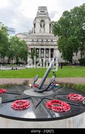 Memorial For Merchant Seafarers, surrounded by poppy wreaths, stands in front of a grand historic building in a green park Stock Photo